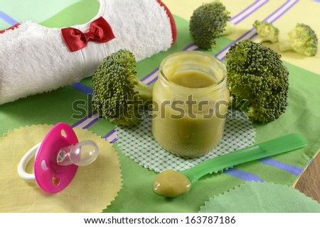 Baby food still life with broccoli puree and bib on green tablecloth