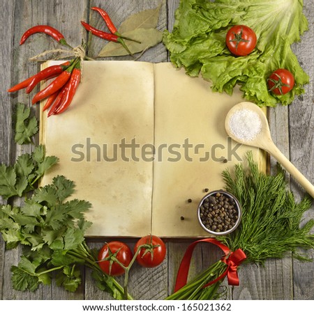 Open cook book with tomatoes, herbs and spices on wooden background