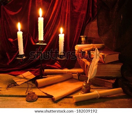 Historical still life with old books, written implements and burning candles in candlelight