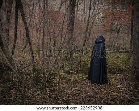 Scary figure in black mantle in the forest, desaturated image