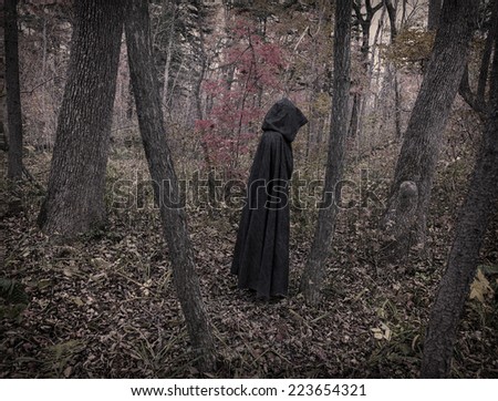 Scary figure in black mantle in the autumn forest, desaturated image