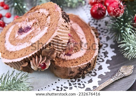 Chocolate rolled cakes with cream and berry jam on wooden plate with white napkin, close up. Christmas and New Year celebratory food still life