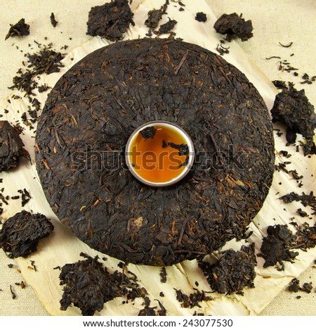 Pressed cake of Asian pu-erh tea with clay cup full of hot tea in the middle, on paper background