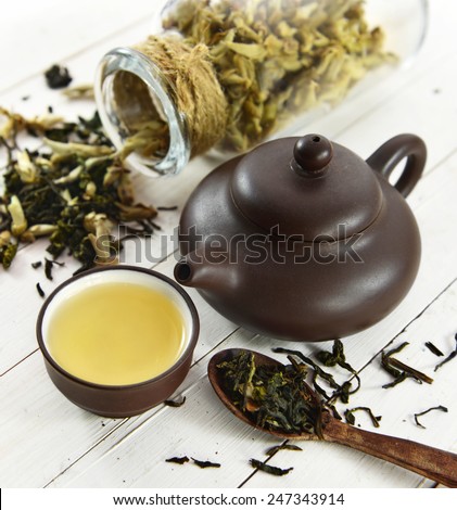 Still life with small cup of green tea, brown tea pot and spoon full of raw tea leaves, chinese tea concept