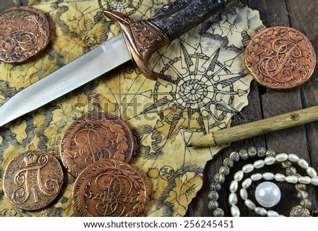 Pirate still life with decorated dagger, map, ancient coins and pearl necklace on wooden background