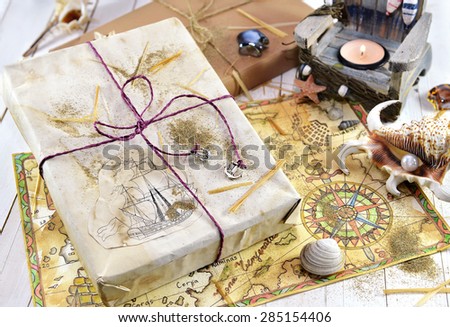 Wrapped gift with hand drawn pirate map, shells and burning candle, holiday still life