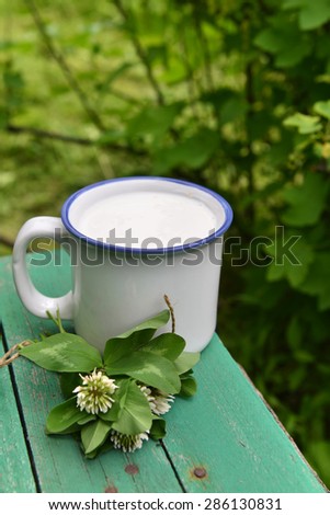 Still life with mug of milk and clover bunch on green wooden planks over summer background