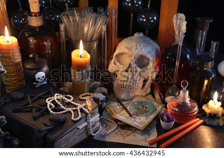 Scary still life with tarot cards, skull, old book, vintage bottles and candles on witch table. Halloween or esoteric concept. Black magic and occult objects in evil interior
