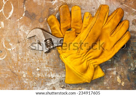 Old workbench with spanner and two yellow work gloves on worn surface.