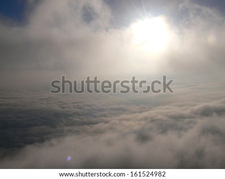 The sun glows through fog over dense clouds.