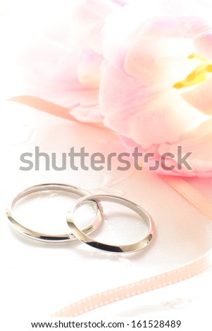 Two wedding bands laying together beside a piece of ribbon and flower petals.