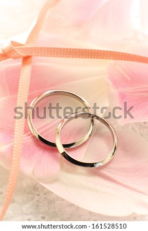 Two wedding bands are laying on flower petals.