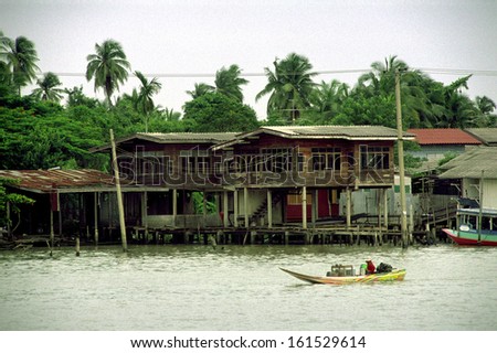 A lone boat passes by a river community set in between palm trees.