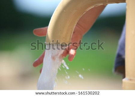 A child\'s hand reaching out to touch the water pouring out of a water pump.