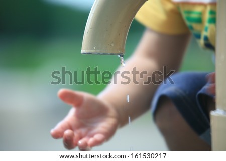 A child reaching under a dripping water faucet.