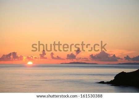 The sun setting by the ocean and some islands.