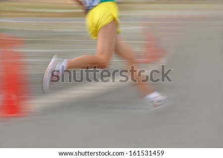 Motion blur of a man in yellow running shorts sprinting on pavement.