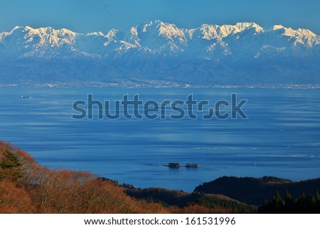 A large body of water surrounded by grassy hills in the foreground and snow capped peaks in the background.