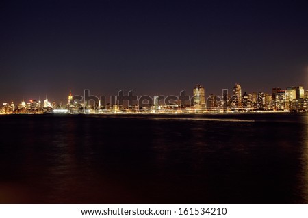 A city skyline illuminates the night sky and reflects on the water.