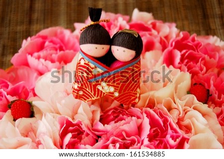 A pair of dolls sit on top a bed of white and pink colored flowers.