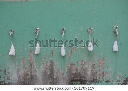 A line of faucets sit on a rusting background with white sacks hanging from each.