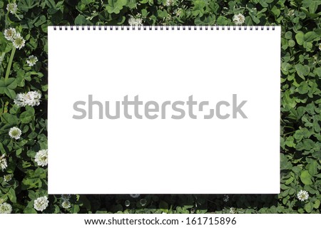 A blank coiled notebook surrounded by green foliage.