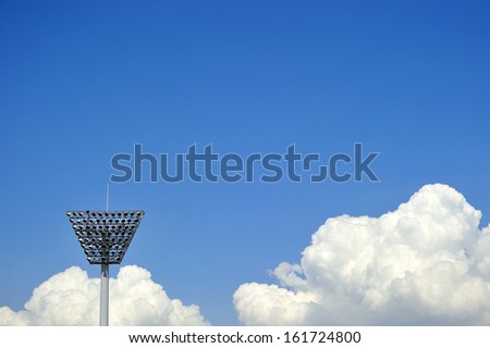A large metal tower reaches above the clouds into a vivid blue sky.