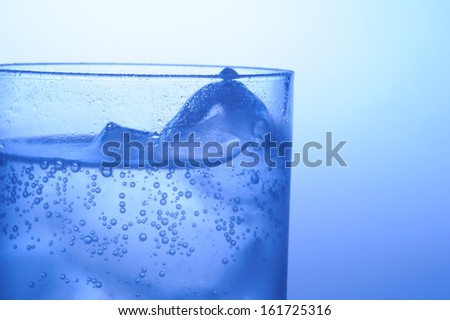 A glass filled with ice cubes and a carbonated clear beverage.
