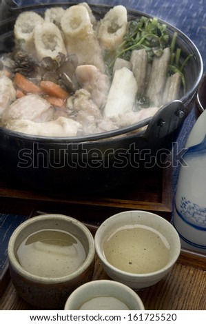 A steaming black pot filled with vegetables and seafood with sauces on the side.