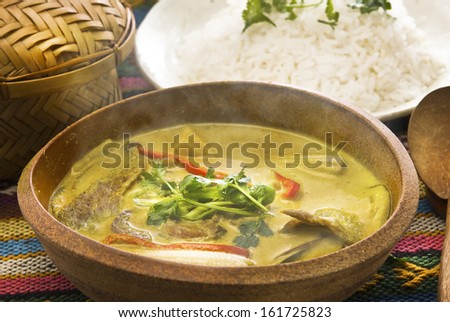 A bowl of steaming soup with rice on a dish behind it.