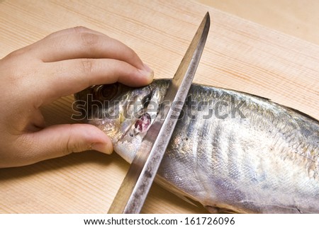 A hand holding a fish head to be cut with a knife.