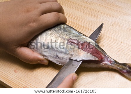 Hands filleting fresh fish on a wood cutting board.