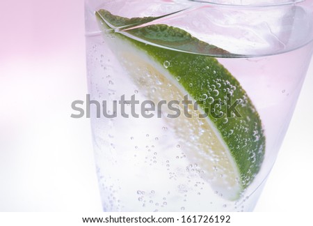 A wedge of lime floating in a glass of clear carbonated beverage.