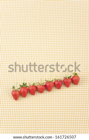A row of strawberries on a yellow gingham background.