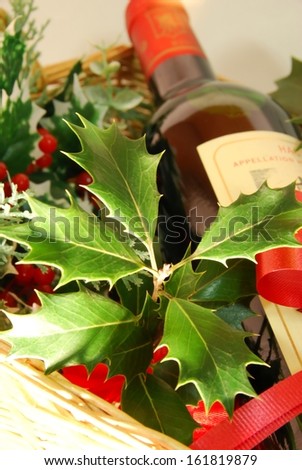 Holly leaves poke out of a wooden gift basket containing a bottle of wine.