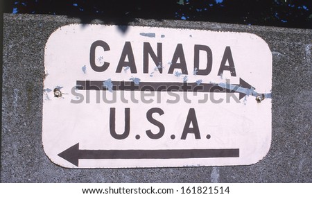 A small white sign with arrows and country names on it.