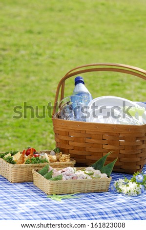 Picnic basket with cutlery and food on blue drop cloth.