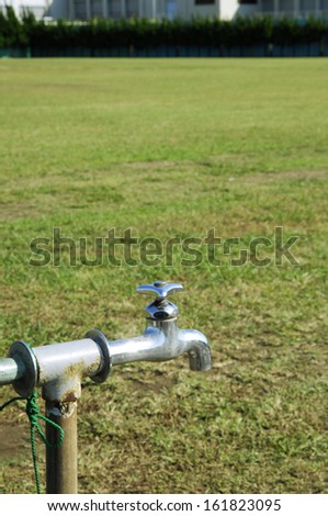 Rusty sprinkler faucet next to dry grass.