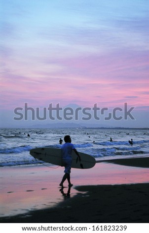A man walking on the beach with a surf board.