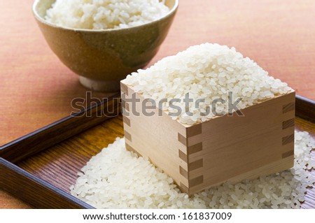 Close-up of raw white rice with bowl of boiled rice