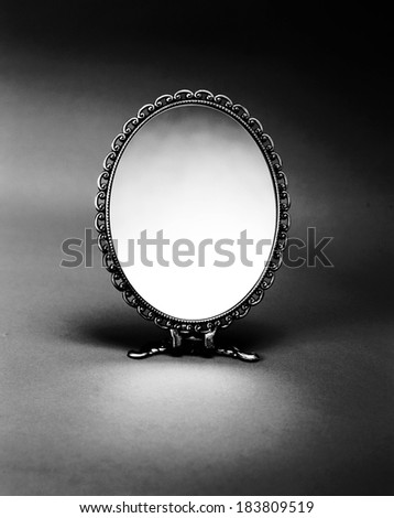 Black and white image of an oval mirror standing on two metal legs.