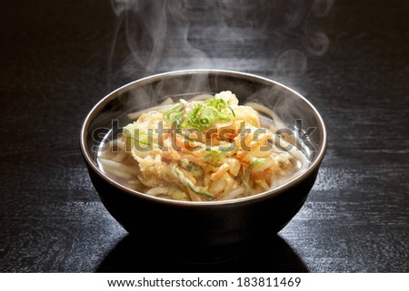 A steaming black bowl of pasta on a wooden table.