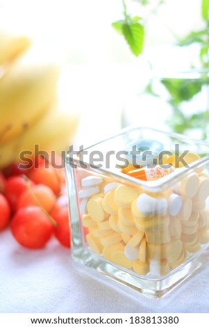 A clear dish full of candy and medicine with tomatoes beside it.