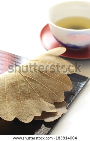 A folded leaf sitting on a tray beside a cup of liquid.