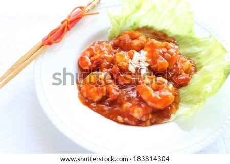 Some shrimps in sauce sitting on lettuce in a white plate.