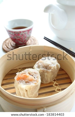 Two wonton in a wooden tray next to a cup of tea and teapot.