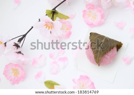 Lots of pink and white flowers scattered on a surface, pink bean paste wrapped in a leaf.