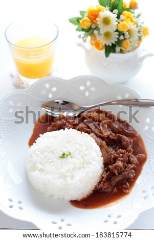 A beef and rice meal served alongside a glass of juice and spring flowers.