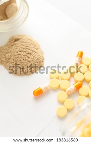 Yellow tablets and capsules lying beside a pile of brown powder.