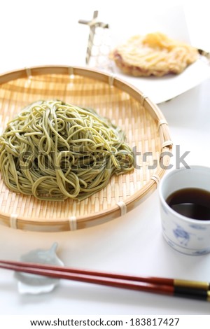 A woven basket filled with green noodles with a cup of tea.